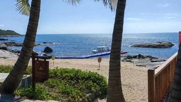 A beach with palm trees, a rocky shoreline, and a boat in the water.