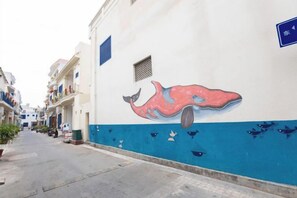 Una calle estrecha flanqueada por edificios, uno de ellos con un mural de una ballena y peces.