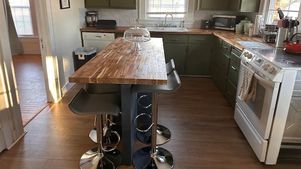A kitchen with a wooden island, stainless steel appliances, and green cabinets. - Holmes Residence (Taylorsville)
