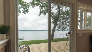Ein Zimmer mit einer Schiebetür, die auf eine Terrasse mit Seeblick und Bäumen führt.