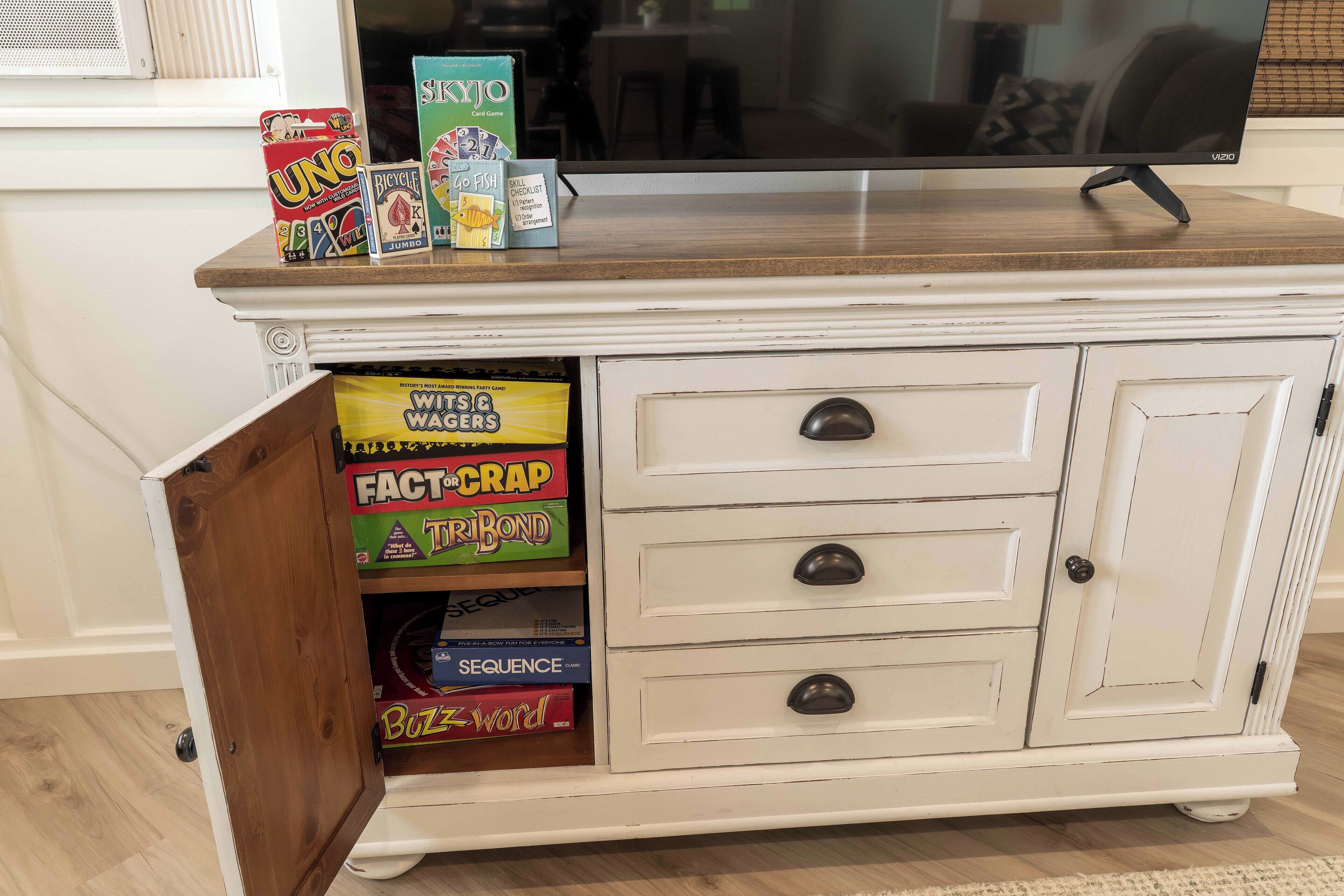A white cabinet with a wooden top shelf holding board games.