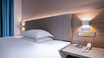 A hotel room with a bed, bedside table, phone, and wall-mounted light fixture.