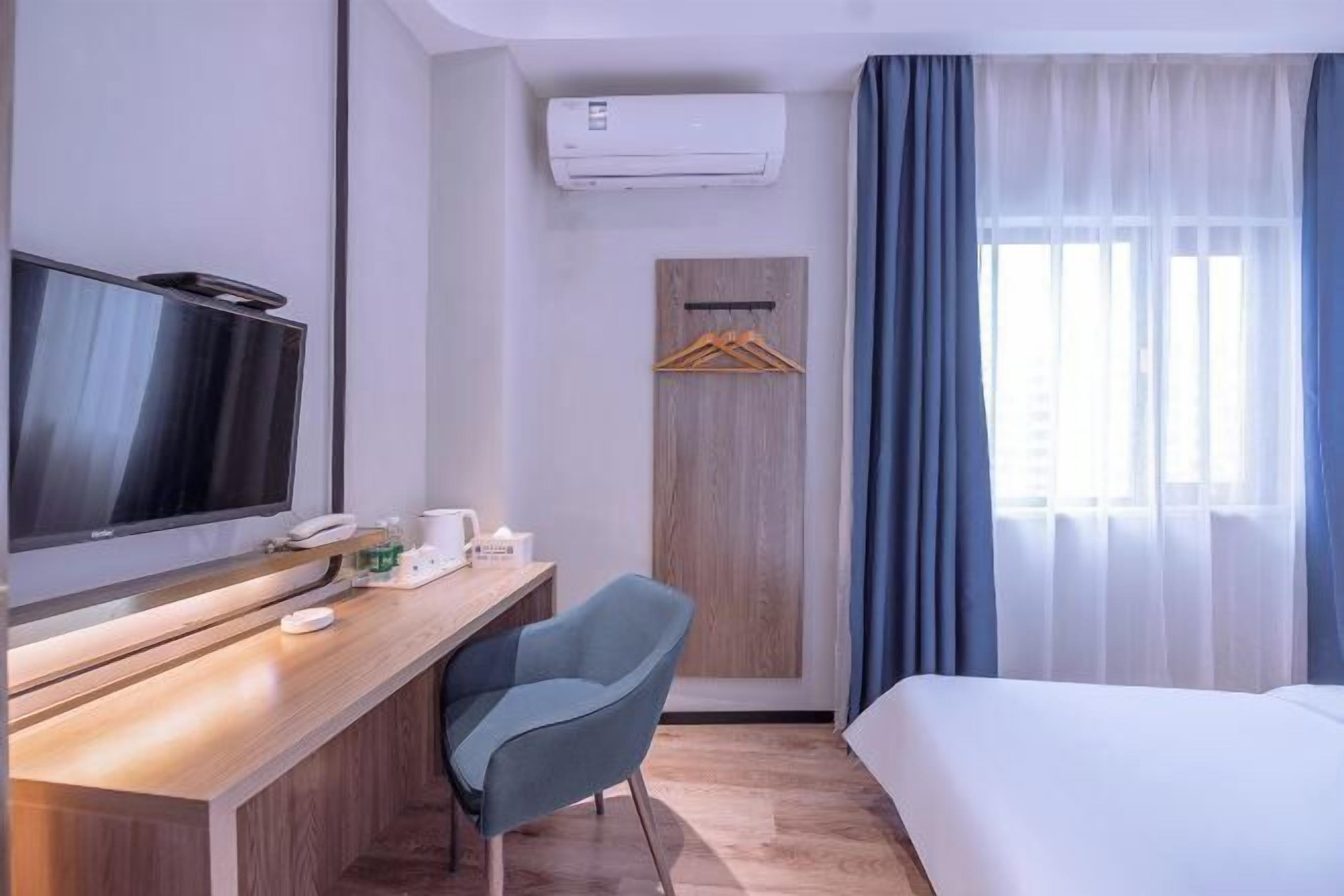 A hotel room with a bed, a desk with a television, a chair, a wardrobe, and a window with curtains.