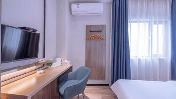 A hotel room with a bed, a desk with a television, a chair, a wardrobe, and a window with curtains.
