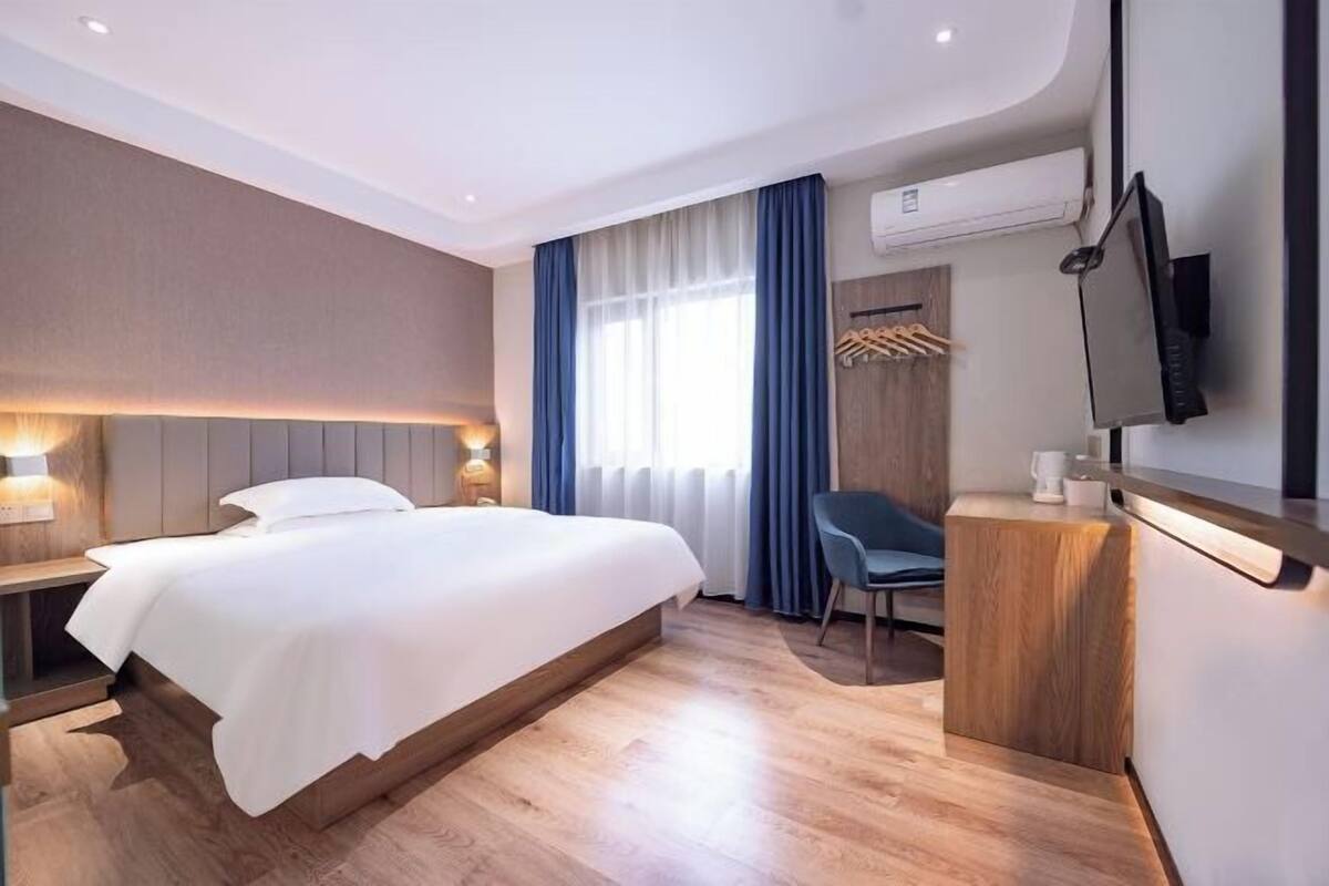 Moderni hotellihuone, jossa on suuri sänky, yöpöydät, työpöytä, tuoli ja seinälle asennettu televisio.