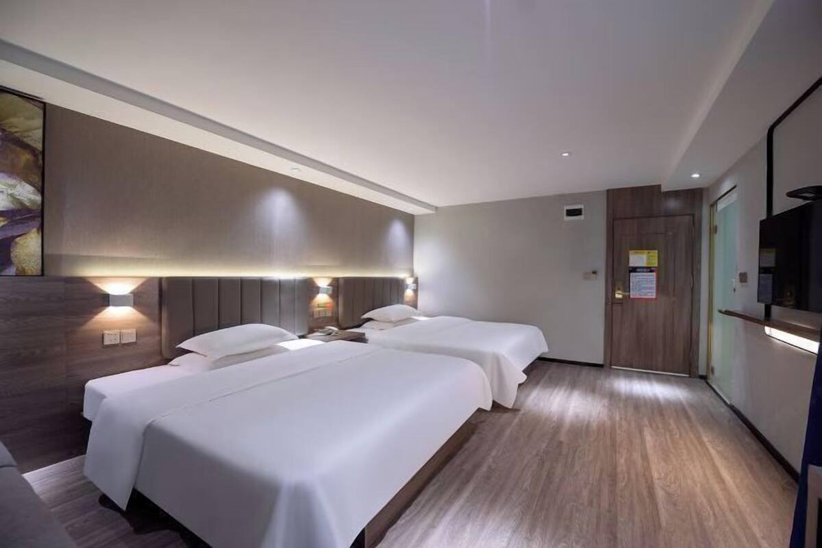 Hotellihuone, jossa on kaksi sänkyä, puulattia, seinälle asennettu televisio ja ovi, jossa on kyltti.