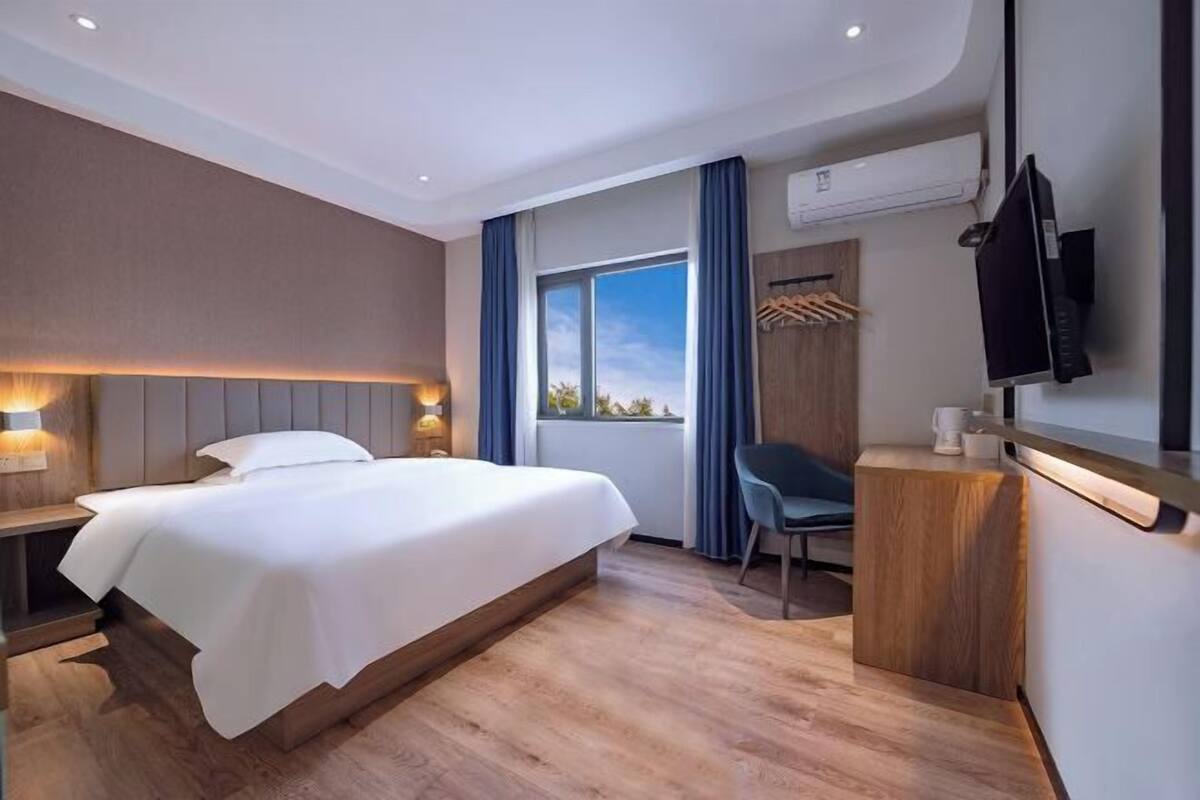 Moderni hotellihuone, jossa on suuri sänky, työpöytä, tuoli, televisio ja ikkuna, jossa on verhot.