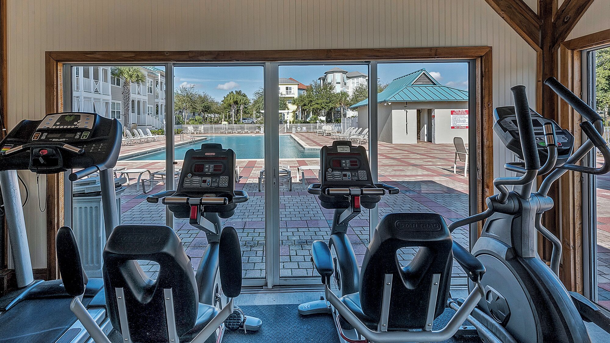 An indoor gym with cardio machines and a view of a pool and buildings outside.