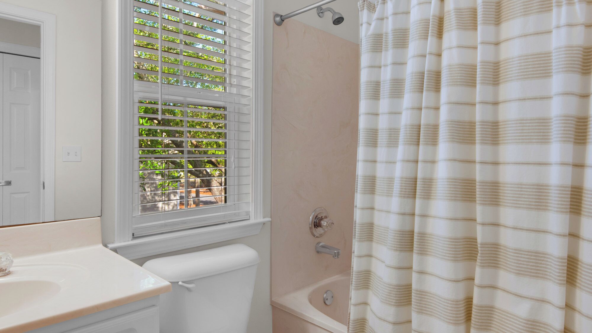 A bathroom with a toilet, sink, shower, and window with blinds.