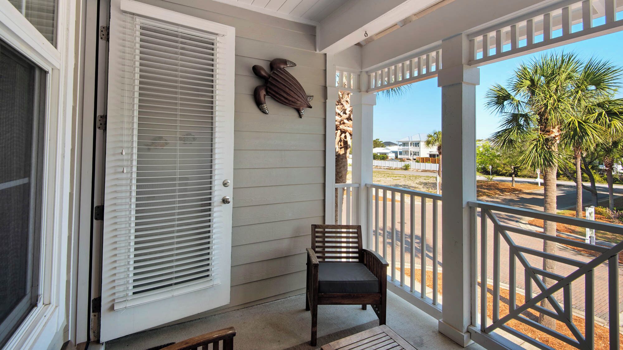 A covered porch with a wooden bench, a decorative turtle sculpture, and a view of a residential area with palm trees.