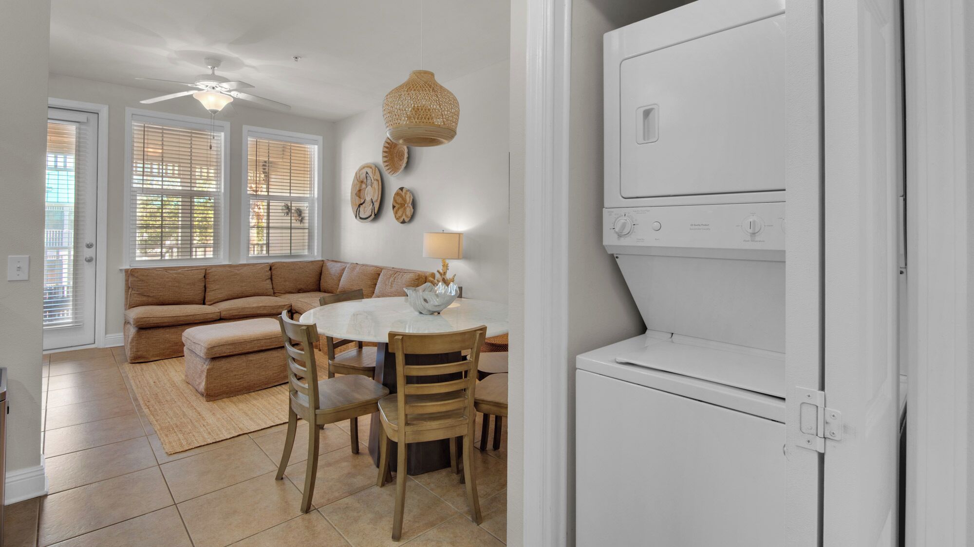 A modern kitchen with a built-in washer and dryer, a dining area with a round table and chairs, and a living room with a sofa and a ceiling fan.