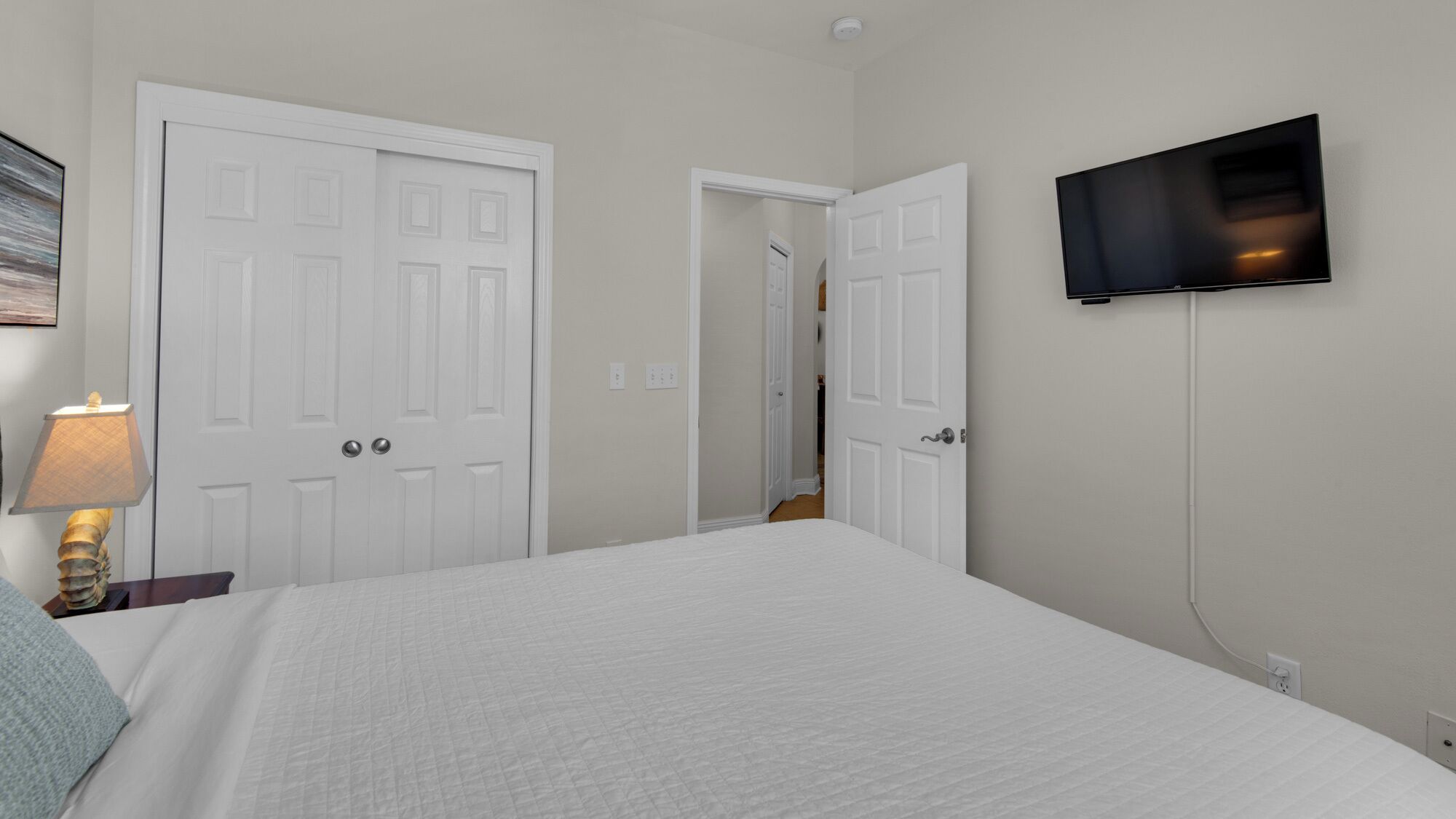 Une chambre à coucher avec un lit, un téléviseur fixé au mur et deux portes blanches.