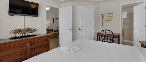 A bedroom with a bed, dresser, TV, and a door leading to a bathroom.