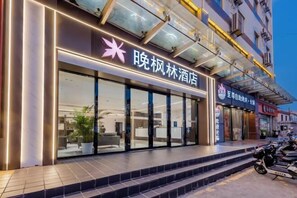 A hotel entrance with a glass facade, a visible reception area, and steps leading up to the entrance. - Wanfenglin Hotel (Shanghai Heqing Meijiayi Plaza Branch) (Shanghai)