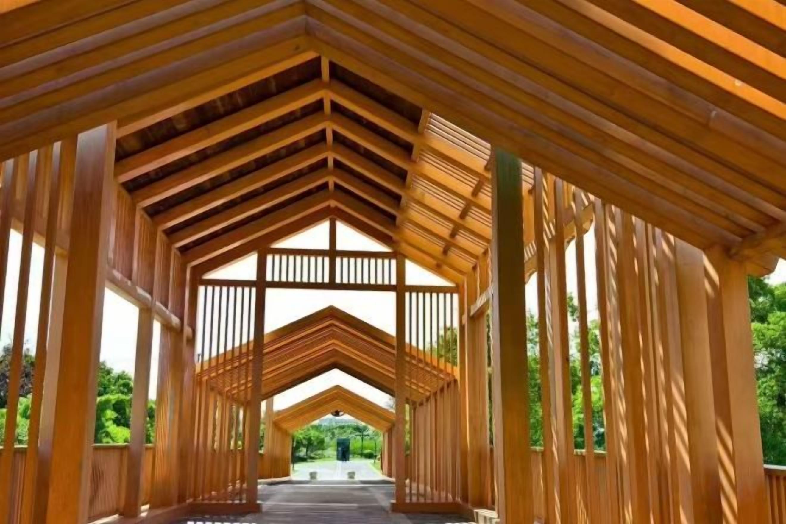 Un pasillo cubierto de madera con una estructura de techo simétrica y laterales abiertos, que conduce a una vista distante.