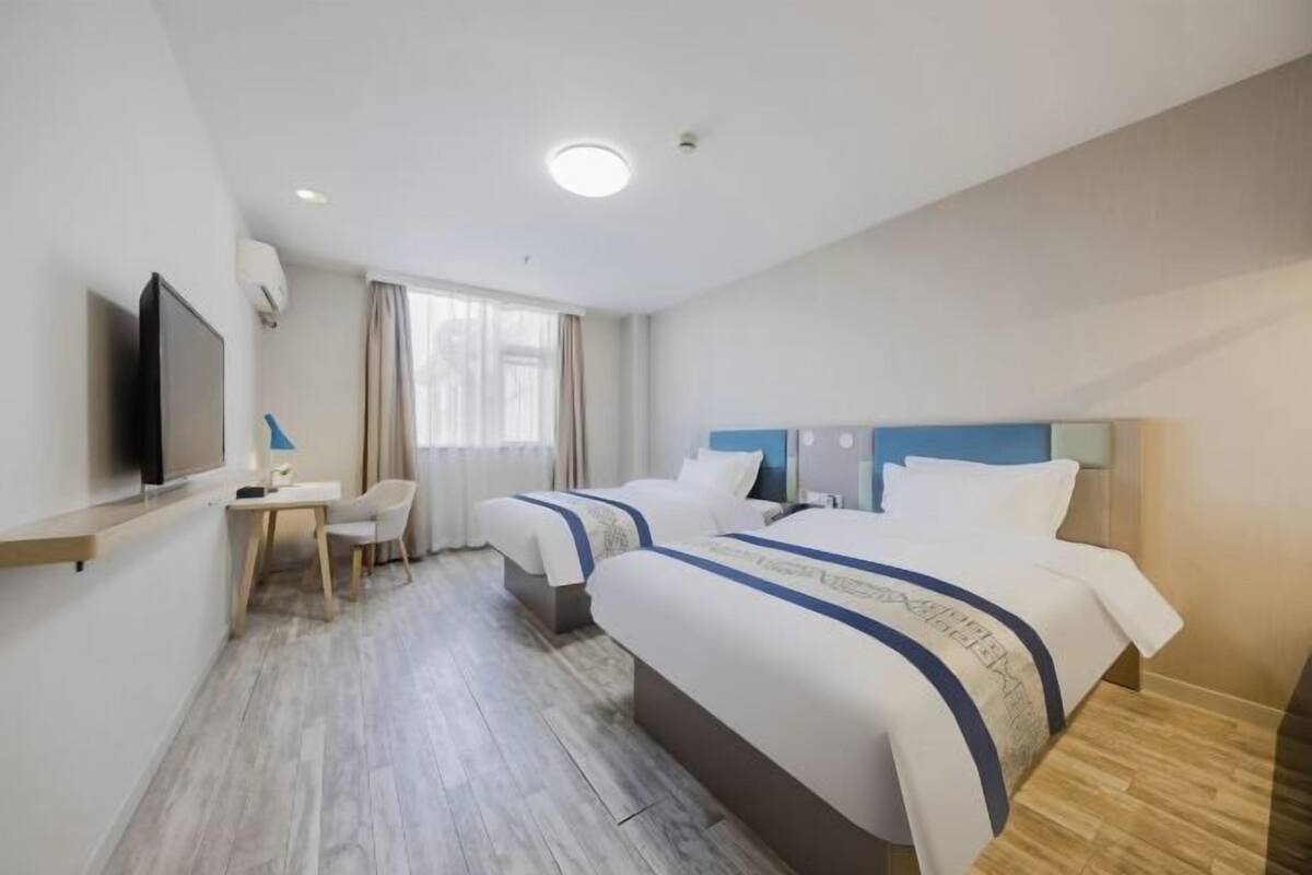 Una habitación de hotel con dos camas, un escritorio, una silla, un televisor y una ventana con cortinas.