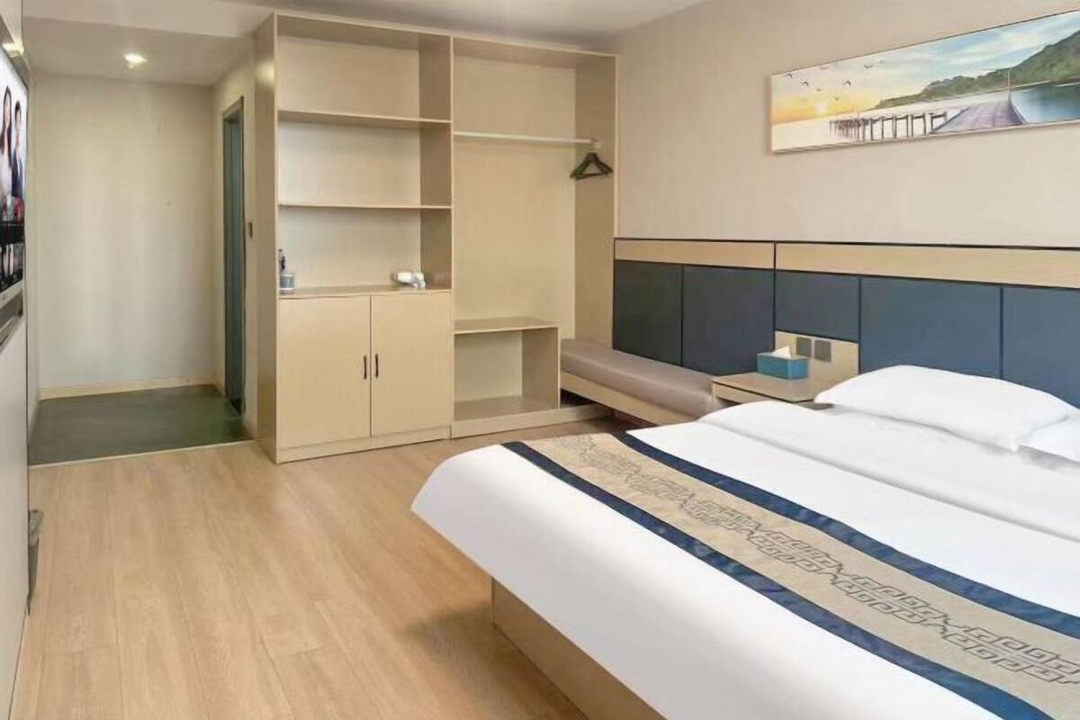 Una habitación de hotel con cama, armario, mesita de noche y un cuadro en la pared.