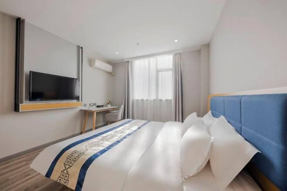 Habitación de hotel con cama, escritorio, televisión y ventana con cortinas.