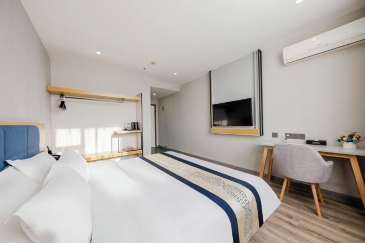 A hotel room with a bed, a desk, a chair, a large mirror, and a wardrobe.
