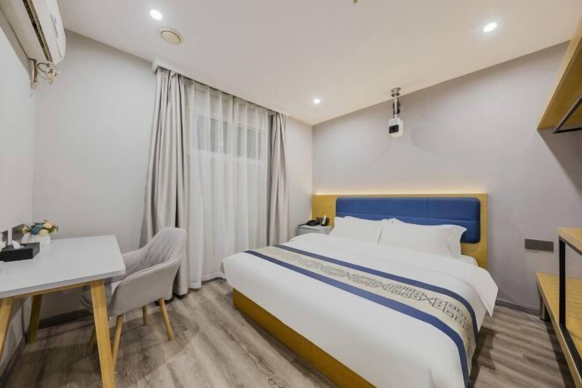 Habitación de hotel con cama, escritorio, silla, mesita de noche y aire acondicionado instalado en la pared.