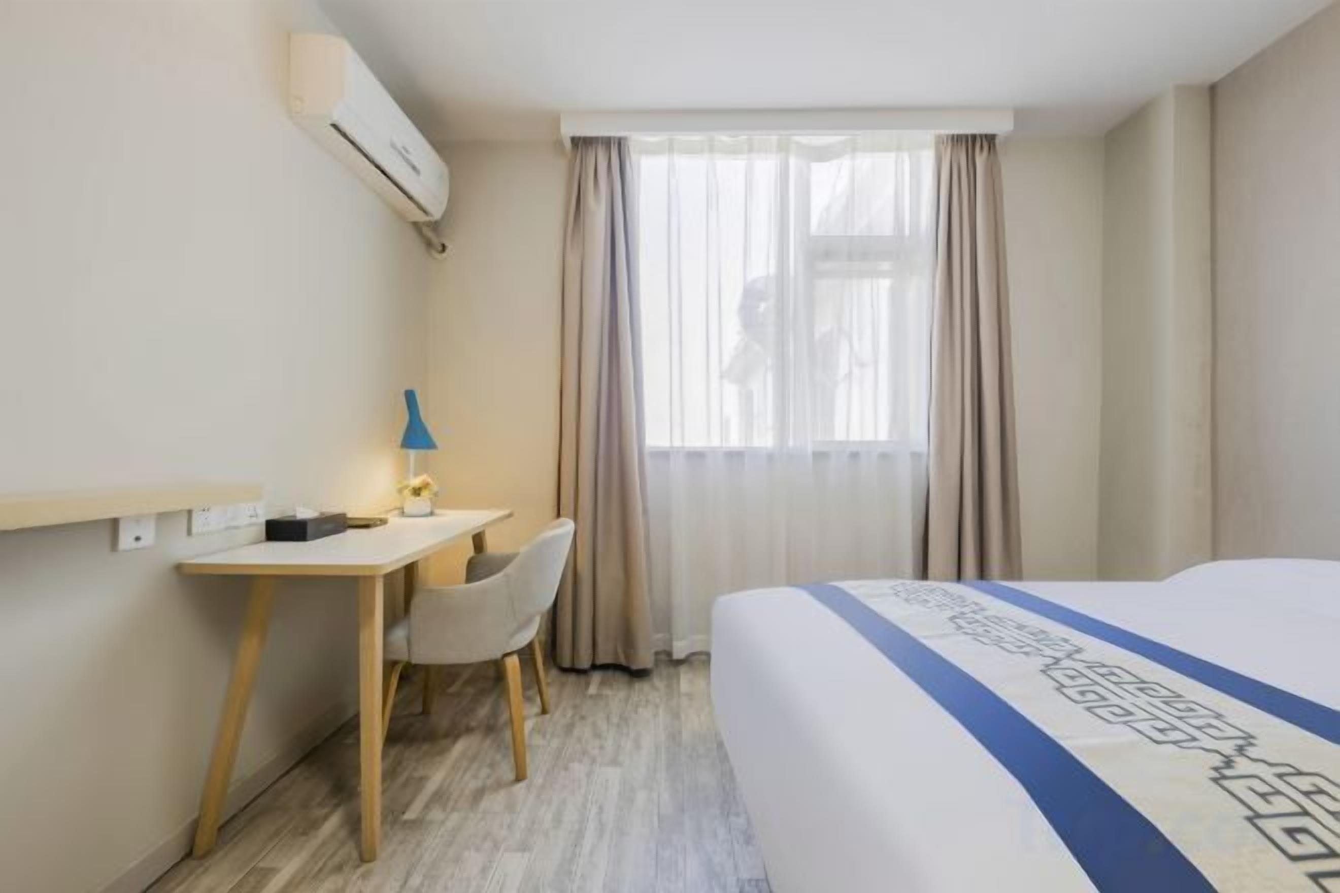 A hotel room with a bed, a desk, a chair, and a window with curtains.