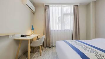 A hotel room with a bed, a desk, a chair, and a window with curtains.