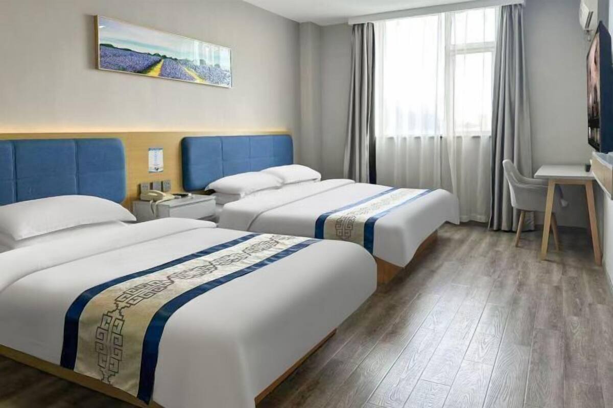 Habitación de hotel con dos camas, un escritorio, una silla, un televisor y una ventana con cortinas.