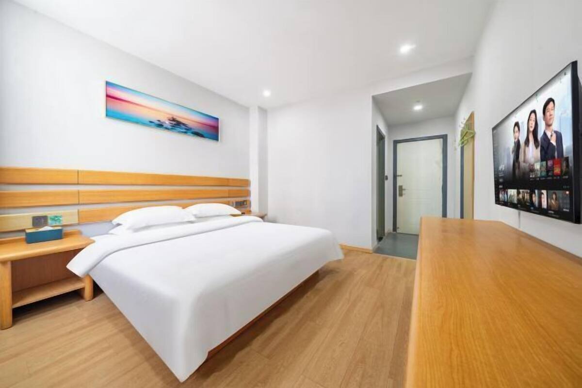 Habitación de hotel con cama, mesita de noche de madera, un cuadro en la pared y una televisión mostrando una película.