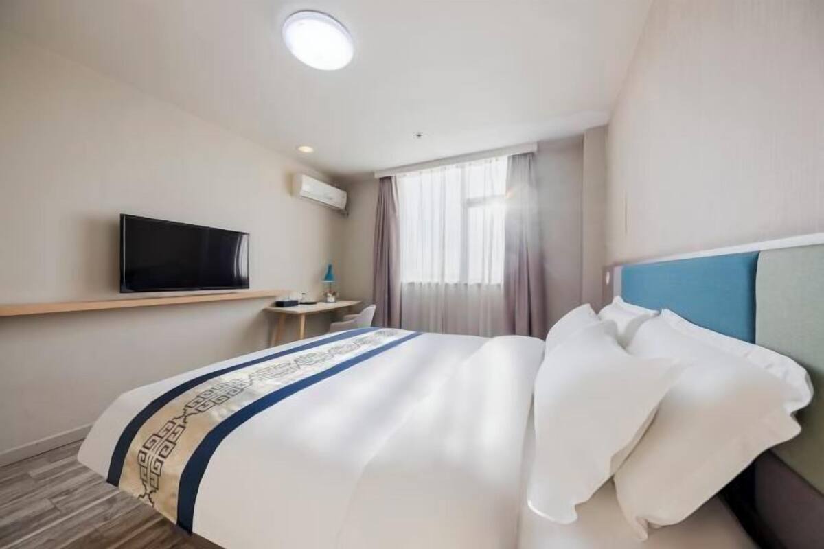 Habitación de hotel con cama, televisión, escritorio y ventana con cortinas.