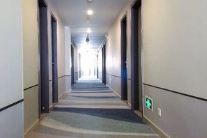 A hotel corridor with a carpeted floor, doors on both sides, and a green exit sign on the wall.