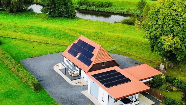 A modern house with a sloped roof, solar panels, and a boat docked outside.