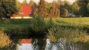 A rural landscape with a house, a pond, and trees.