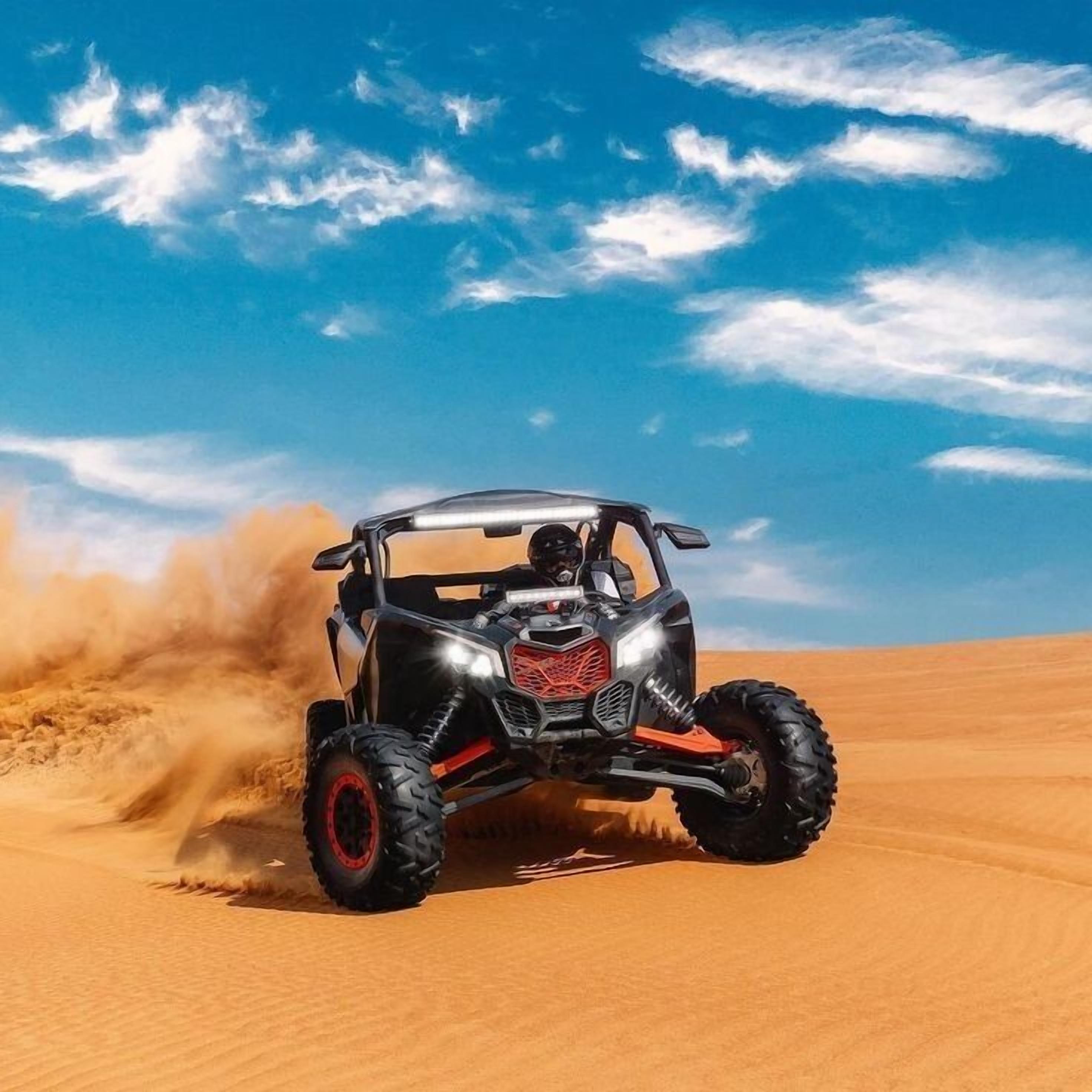 A black off-road vehicle driving through a desert with sand being kicked up behind it.
