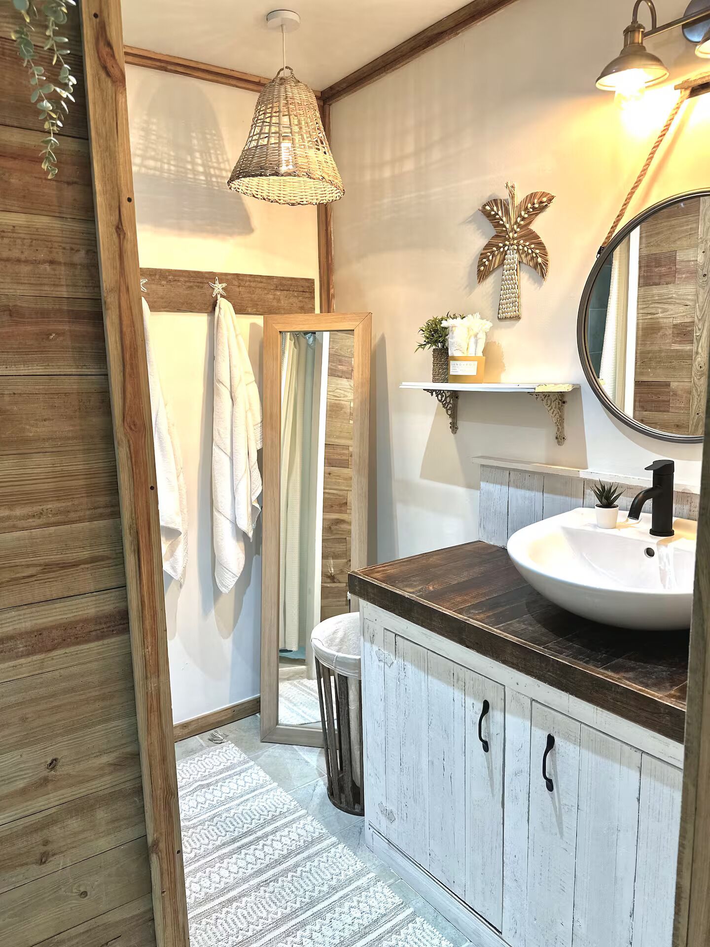 A bathroom with a wooden vanity, a round mirror, a white sink, and a hanging light fixture.