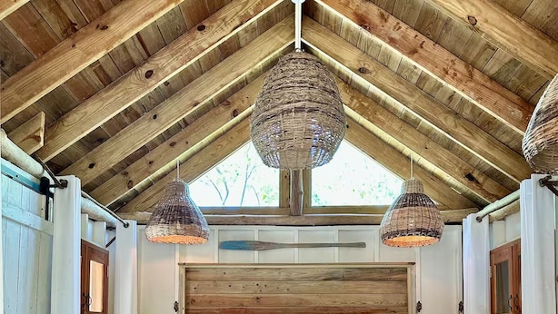 Une chambre à coucher au style rustique, dotée d’un grand lit, de poutres en bois et de luminaires en fibres tressées.