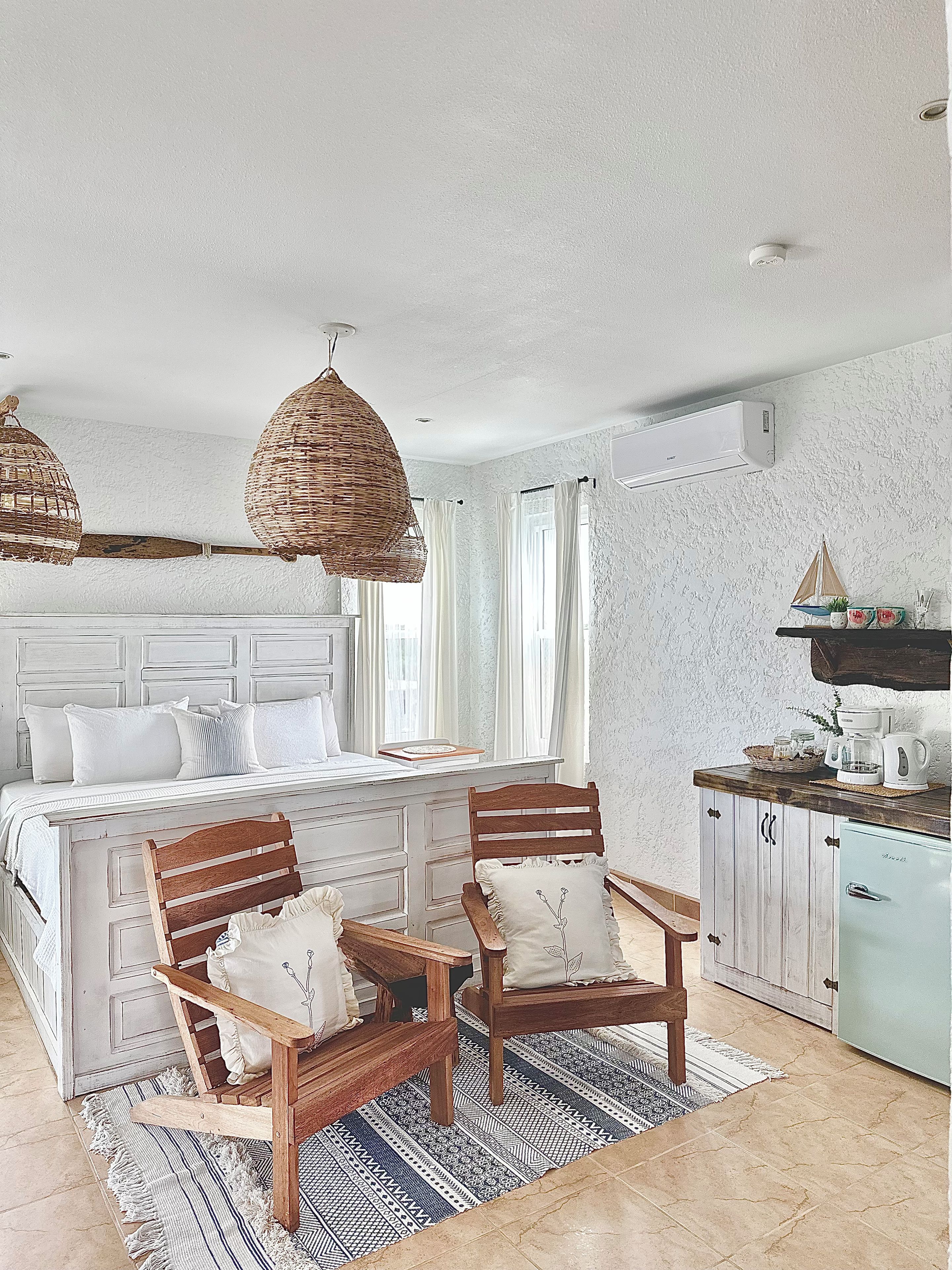 Une chambre avec un grand lit, deux chaises en bois, une petite table et un coin cuisine.