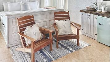 Une chambre avec un grand lit, deux chaises en bois, une petite table et un coin cuisine.