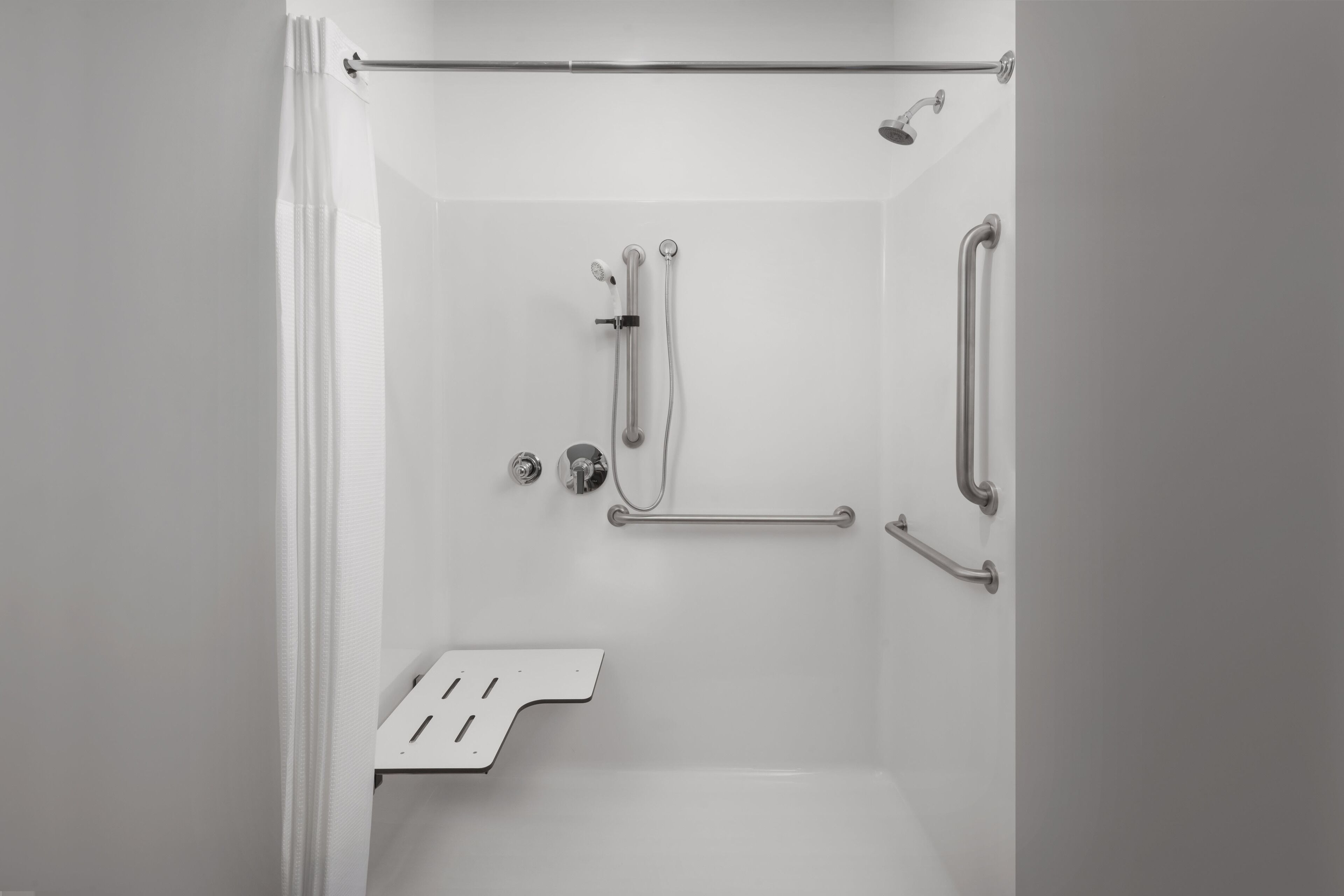 Un espace douche moderne équipé d’une barre d’appui, d’un pommeau de douche et d’un flexible de douche.