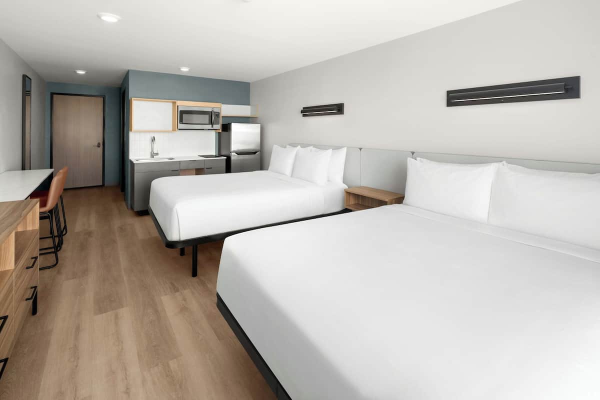 A hotel room with two beds, a desk, a chair, a microwave, and a sink.