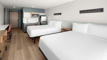 Ett hotellrum med två sängar, ett skrivbord, en stol, en mikrovågsugn och ett handfat.