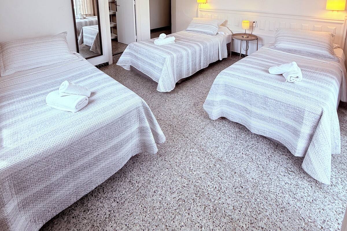 A hotel room with four beds, a mirror, a small table, and a wall-mounted air conditioner.