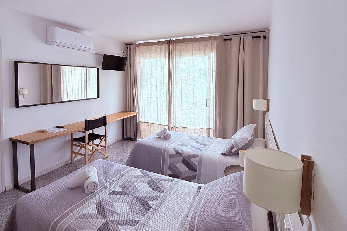 A hotel room with two beds, a desk, a chair, a TV, and a window with curtains.