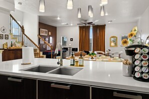 Een moderne keuken met een dubbele spoelbak, een eethoek met tafel en stoelen, een trap en een plafondventilator.