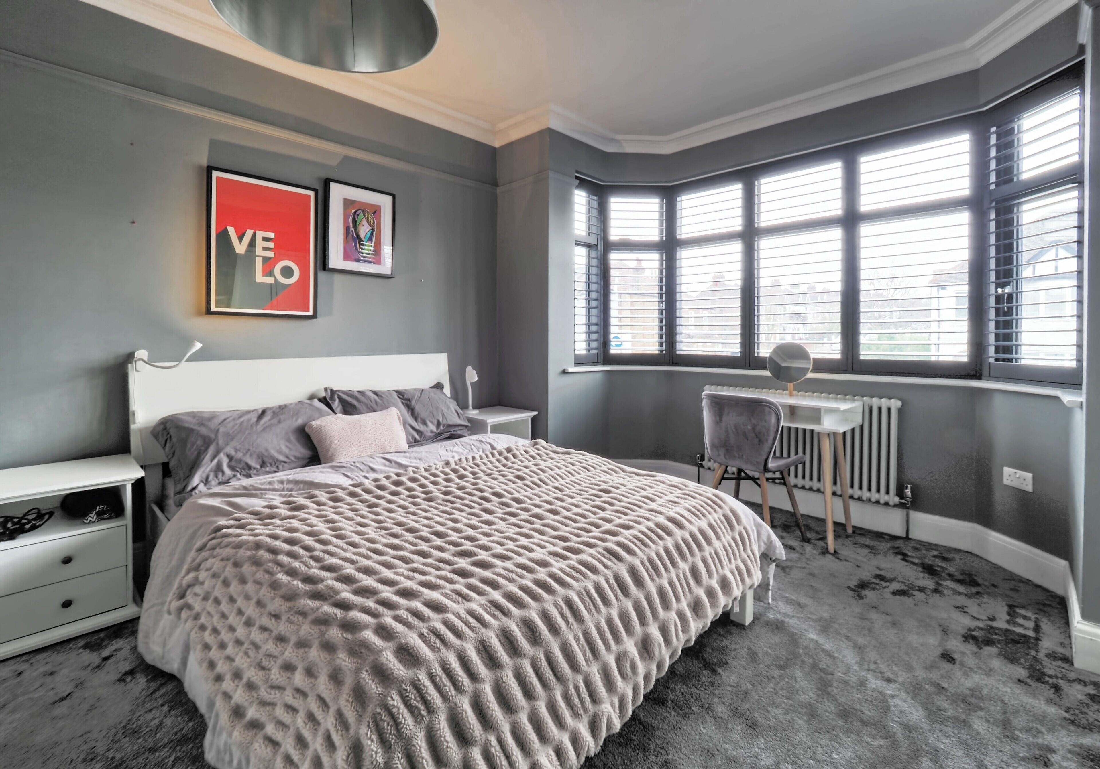 Un dormitorio con una cama grande, una mesita de noche blanca, una silla y un radiador.