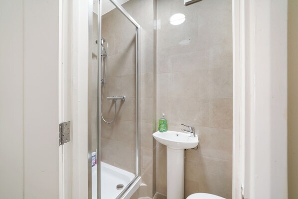 A bathroom with a glass-enclosed shower, a white sink, and a toilet.