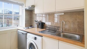 Una cucina compatta con lavastoviglie, lavatrice e finestra con vista sulla città.
