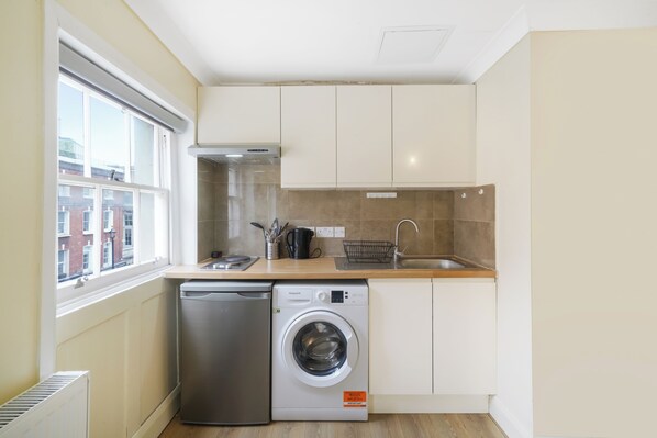 A compact kitchen with a dishwasher, washing machine, and a window with a view of buildings.