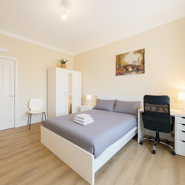 Ein ordentlich eingerichtetes Schlafzimmer mit Bett, Schreibtisch, Stuhl, Kleiderschrank und einem Bild an der Wand.