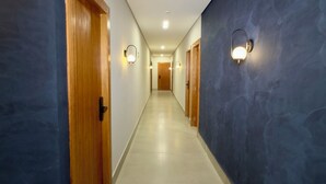 Un long couloir étroit, avec des portes en bois d’un côté et un mur bleu foncé de l’autre, qui mène à une pièce au bout.
