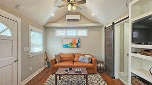 A living room with a brown sofa, a coffee table, a ceiling fan, and a mounted air conditioner. - Private Atlanta Tiny House with 
Mini Golf Course (Forest Park)